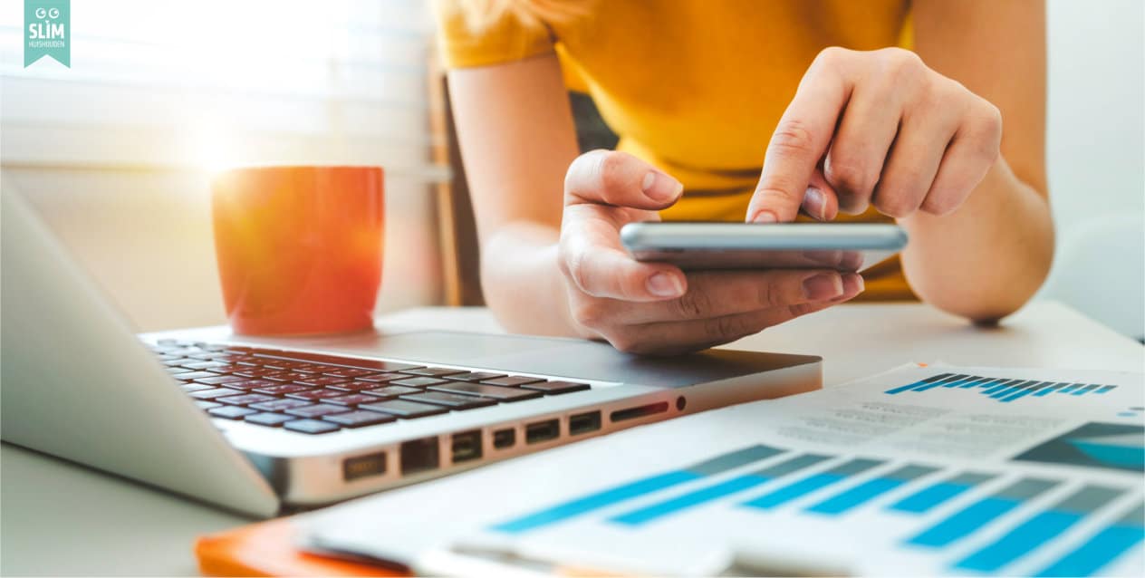 Vrouw die vaste lasten vergelijkt op telefoon en laptop aan de keukentafel | Slim Huishouden