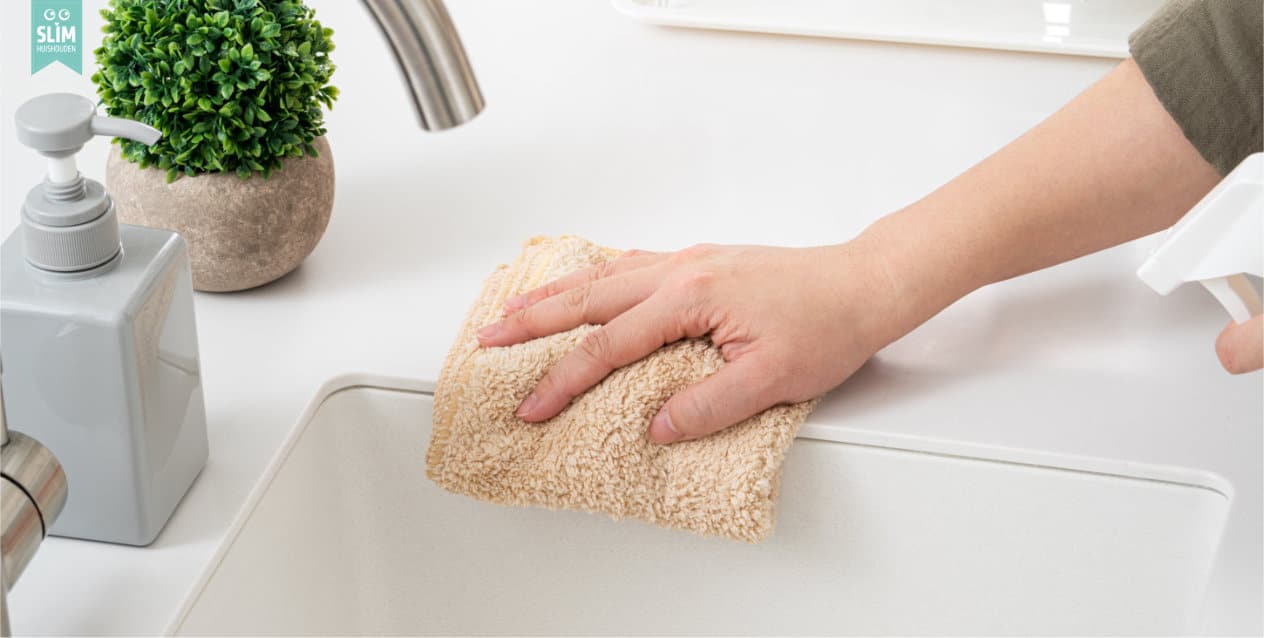 Hand maakt keukenblad schoon met doek en spray