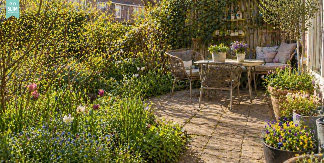 Blog Tuinklusjes Zonnige achtertuin met ruim terras, tuintafel en voorjaarsplanten die los door elkaar groeien