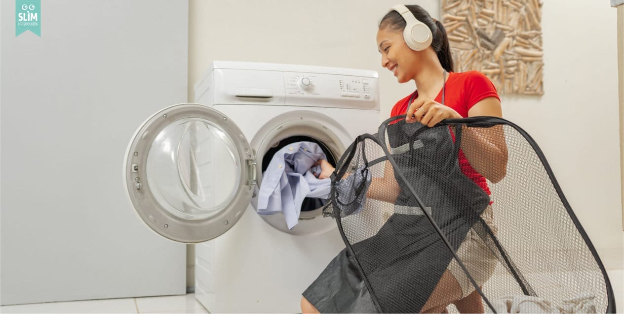Vrouw doet de was en stopt kleding in de wasmachine terwijl ze een koptelefoon draagt 